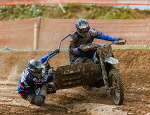 Dynamic sidecar motocross race with two riders tackling a muddy track, showcasing competition and skill.
